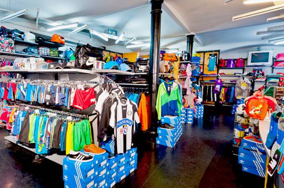 Sportgeschäft mit Regalen voller Sportbekleidung, einschließlich Trikots, Hosen und Accessoires in verschiedenen Farben und Designs.