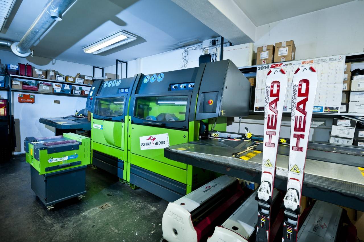 Moderne Ski-Wartungsmaschine in Sporthaus Stückler's Werkstatt mit Ski von HEAD im Vordergrund, die zur Wartung bereitstehen.